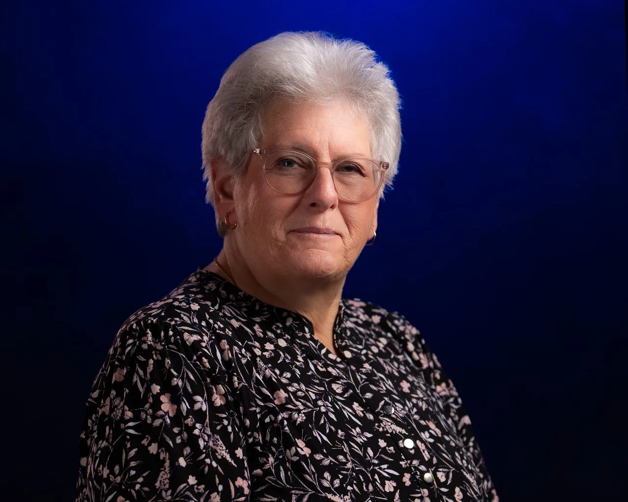 LinkedIn-ready studio headshot of a professional woman in glasses on a deep blue backdrop, Connecticut