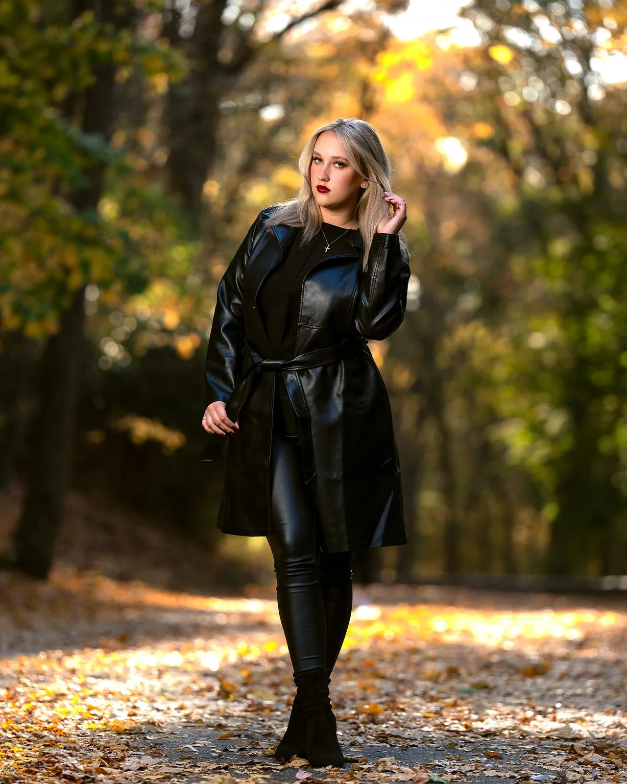 Full-length autumn portrait of a blonde woman in a black leather trench coat among golden fall foliage, CT