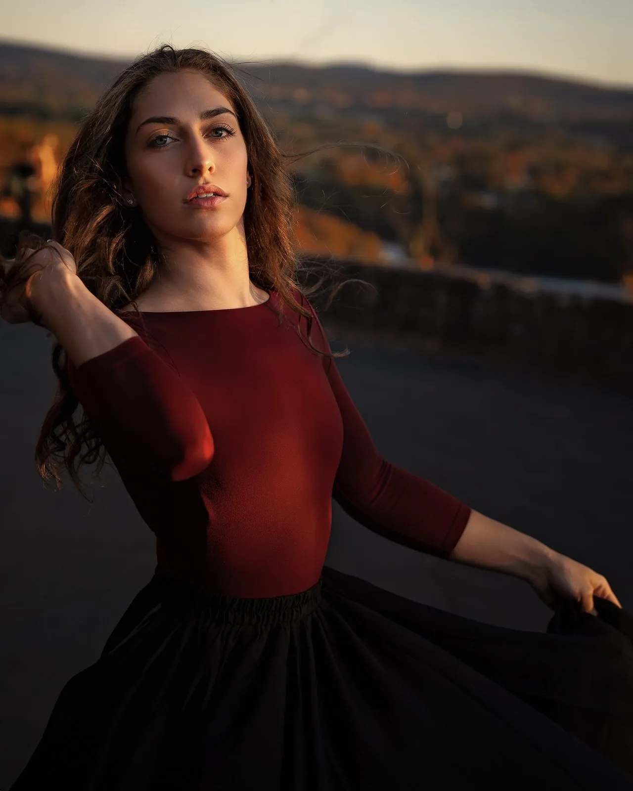 Golden-hour dance portrait of a young woman in a burgundy top on a hilltop overlook at sunset, Connecticut