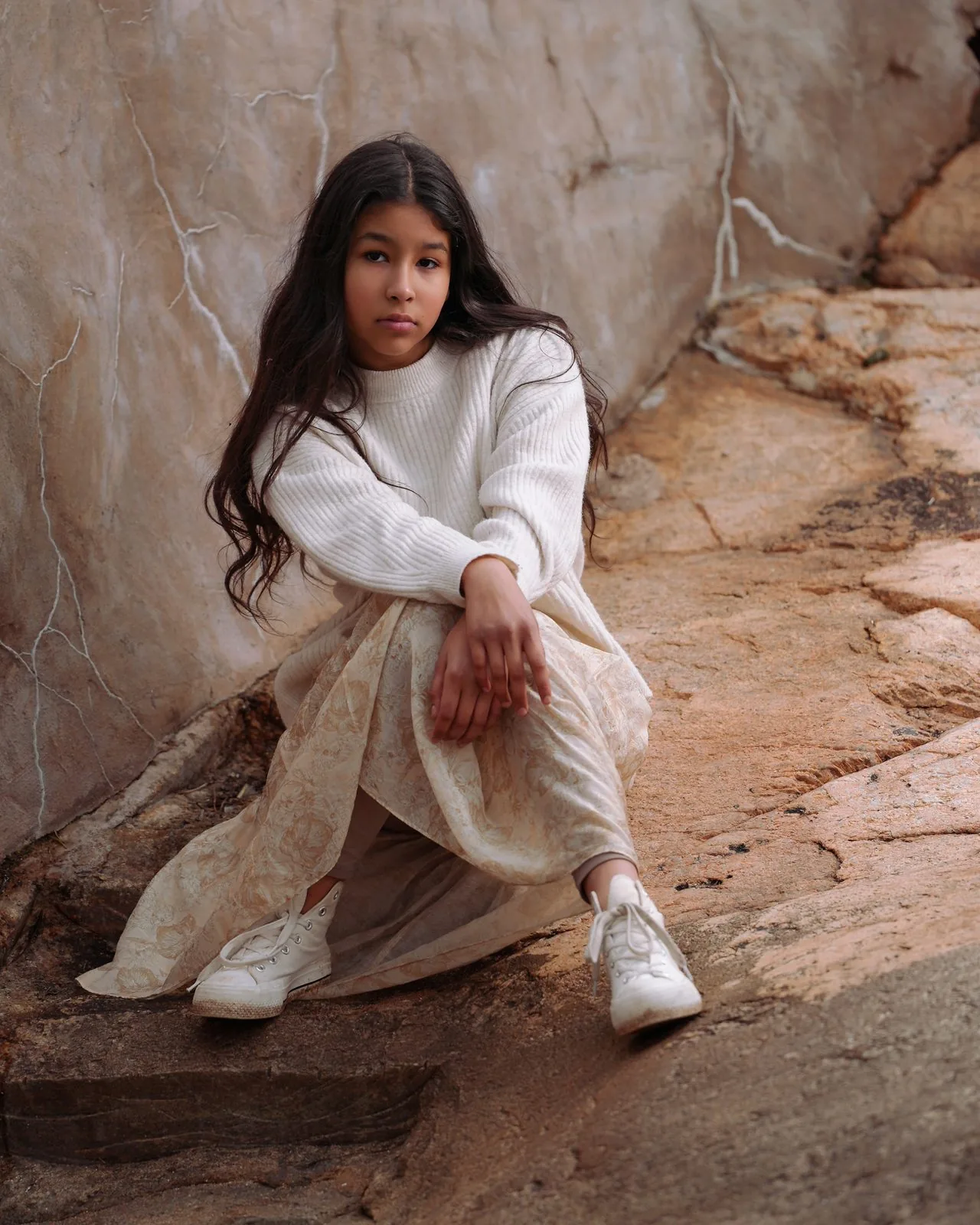 Natural-light senior portrait of a student in a cream sweater seated on sandstone rocks, Connecticut